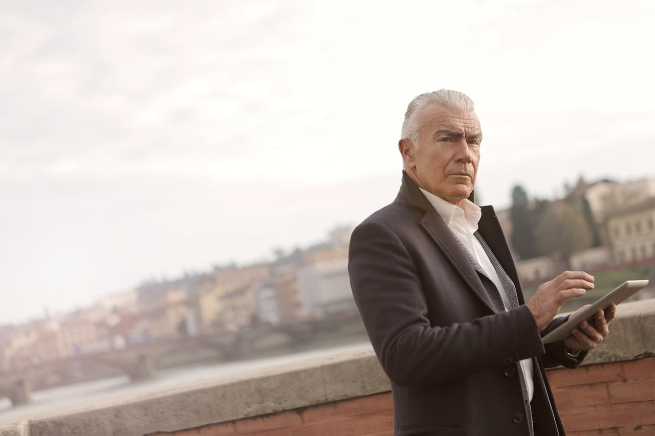 Elderly Man in Black Coat Standing Near Brown Concrete Wall